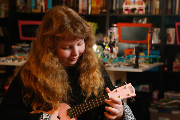 Photo of Charlie Lowthian-Rickert smiling and playing her ukulele.