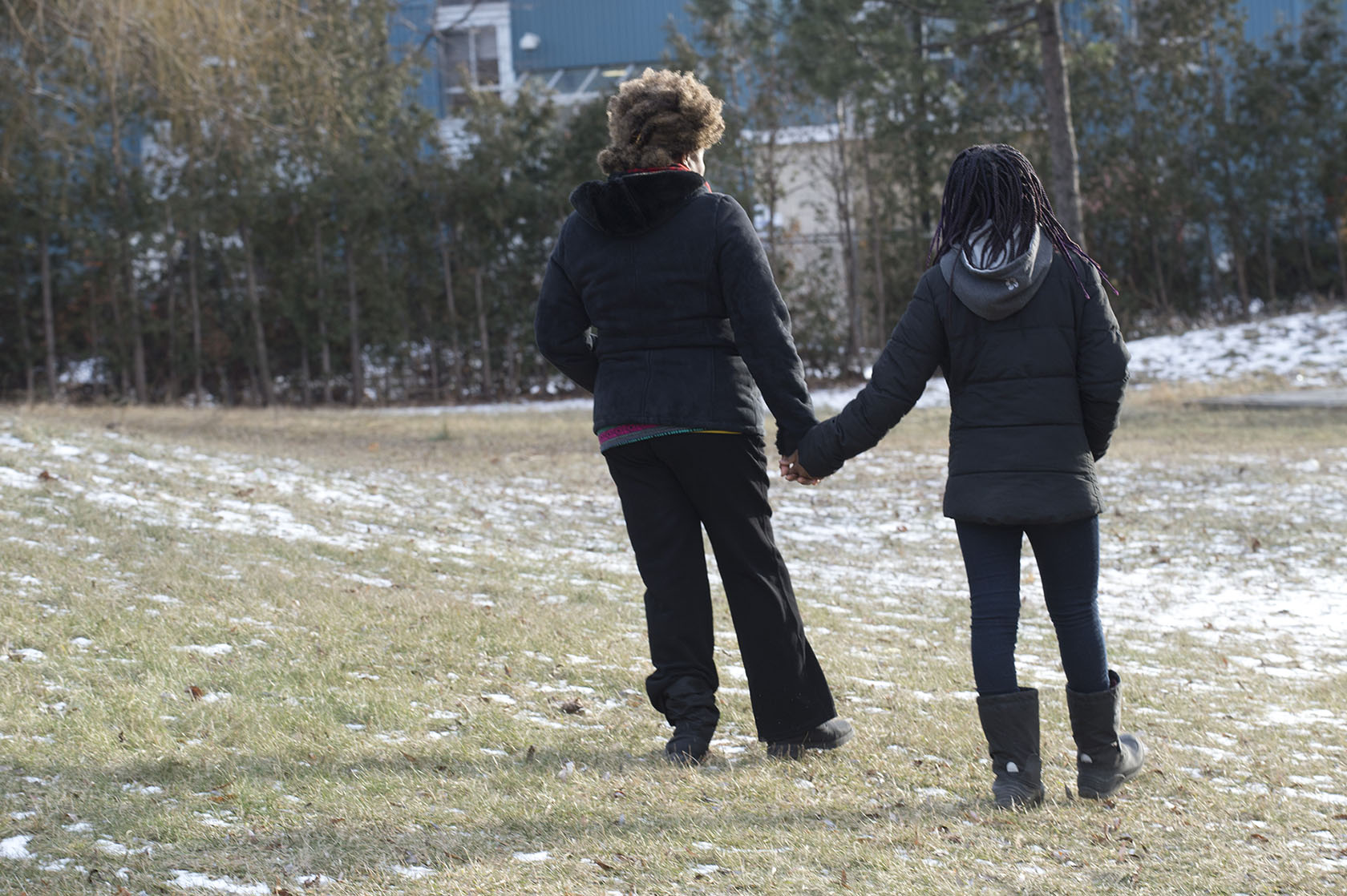 Photo of anonymous mother and daughter (“Jane and Kobina”) holding hands in outdoor setting, with backs to the camera.

